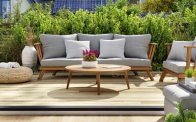 très beau salon de jardin confortable avec des coussins et des arbustes derrière